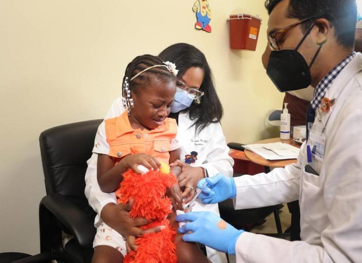 Dr. Nizar Dowla, right, gives a COVID-19 vaccine to Emiola Adebayo, 3, while she sits on the lap of her mother, Dr. Emy Jean-Marie, during a COVID vaccine drive for children younger than 5 on Tuesday, June 28, 2022, at Borinquen Health Care Center in Miami.