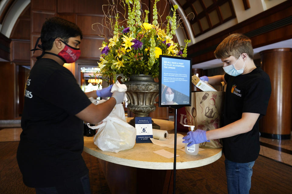 Dhruv Pai, 16, left, and Matthew Casertano, 15, both of North Potomac, Md., wipe down groceries with disinfectant as they deliver them to David Benkin, 85, and Rebecca Adler, 81, Wednesday Aug. 19, 2020, in North Bethesda, Md., as part of the nonprofit organization, "Teens Helping Seniors" that Pai and Casertano co-founded. The teens call when they are outside and leave the bags of groceries on a table in the lobby of the building for the seniors to pick up after they leave, in order to minimize the risk of coronavirus exposure for the seniors. (AP Photo/Jacquelyn Martin)
