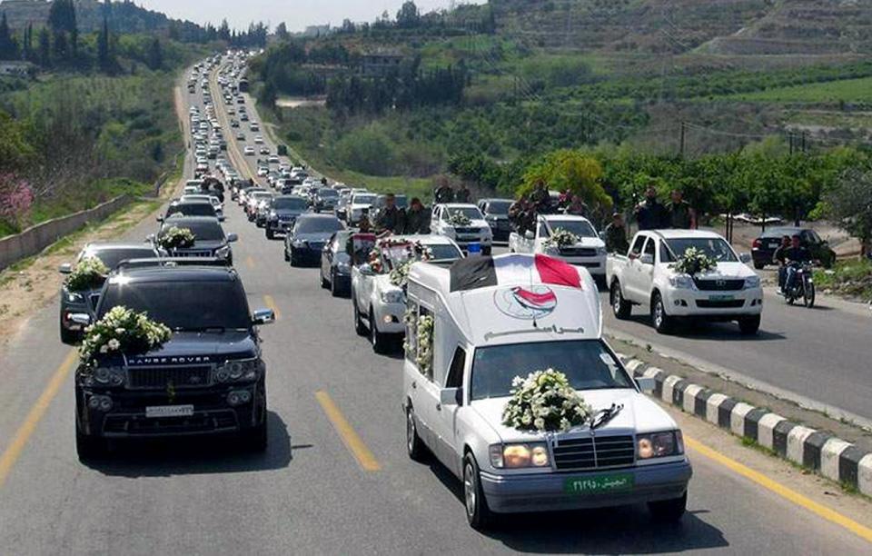 In this Monday, March 24, 2014 photo released by the Syrian official news agency SANA, a convoy carrying the coffin of the commander of the pro-government National Defense Forces Hilal Assad, during his funeral in Latakia province, Syria. State TV reported late Sunday that Hilal Assad was killed in the fighting against opposition fighters in Kassab. The commander was a member of Syrian President Bashar Assad's family but the TV did not say if they were close relatives. (AP Photo/SANA)