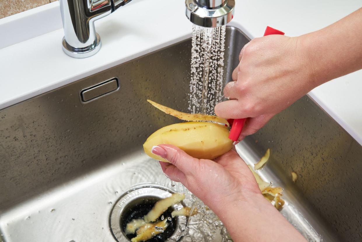 Cropped view of female hands peeling potato over Food waste disposer machine