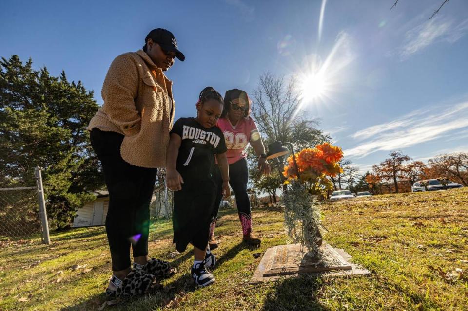 LaKeisha Mackey, middle, prays with her daughter Dererica Johnson, left, and her niece Kenzlee Carson, 5, at her son Derrick Johnson’s gravesite at Cedar Hill Memorial Park in Arlington on Sunday, Dec. 10, 2023. Mackey’s son Derrick was killed in a shooting in 2020 at 19 years of age. Along with her son, she also lost her father in 1989, her uncle in 1980 and her sister in 2017 to gun violence.