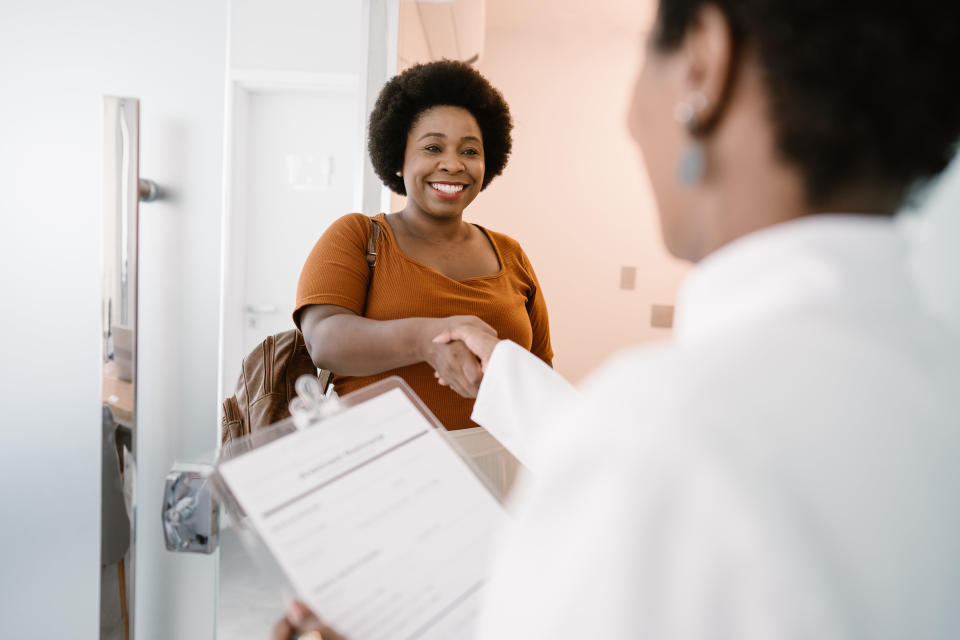 Woman checking in at reception desk, greeted by employee holding a clipboard