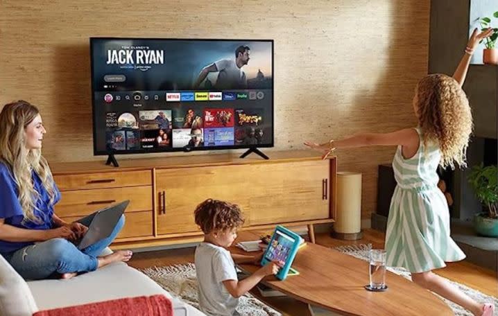 A family plays in a living room with an Amazon Fire TV on the wall.