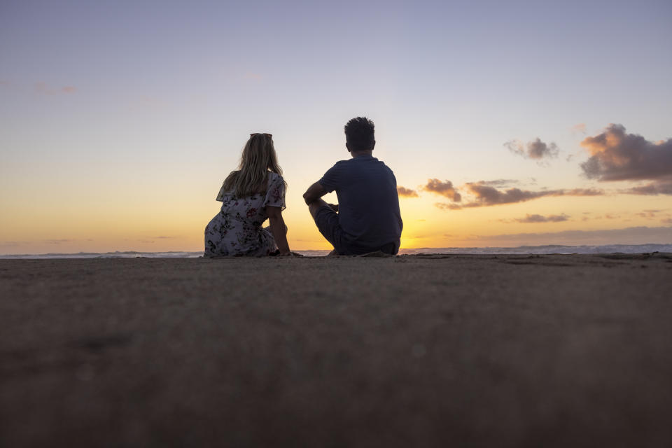 A couple sitting on the beach at sunset