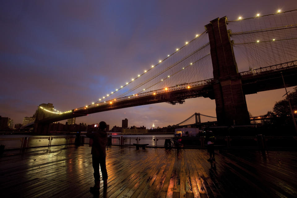 People stop along the Brooklyn waterfront to photograph the Brooklyn Bridge and the Manhattan skyline, Tuesday, Oct. 30, 2012 in New York. Much of lower Manhattan is without electric power following the impact of superstorm Sandy. (AP Photo/Mark Lennihan)