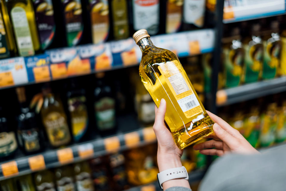 Close up of young woman grocery shopping in a supermarket. Standing by the aisle, holding a bottle of organic cooking oil, reading the nutritional label and checking ingredients at the back (d3sign / Getty Images stock)