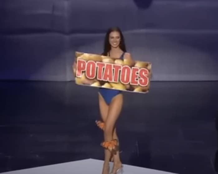 Woman in a dress holding a large sign with the word "POTATOES" on it