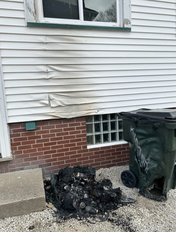 Melted siding from a house on a pile of burned debris next to a dumpster