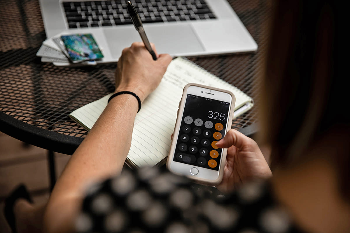 A woman uses a calculator, a notepad and her laptop to work on her finances.