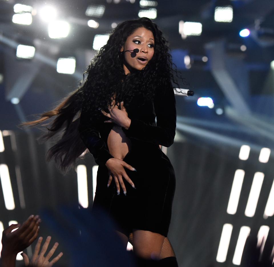 Nicki in a long sleeve black mini dress. She's holding her hands over her chest and crotch to hold together fabric torn down the middle revealing her stomach.