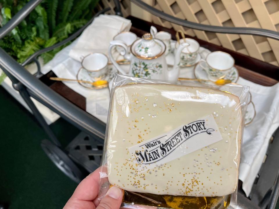 carly holding cookie with main street story logo over a cart with a tea set at disneyland