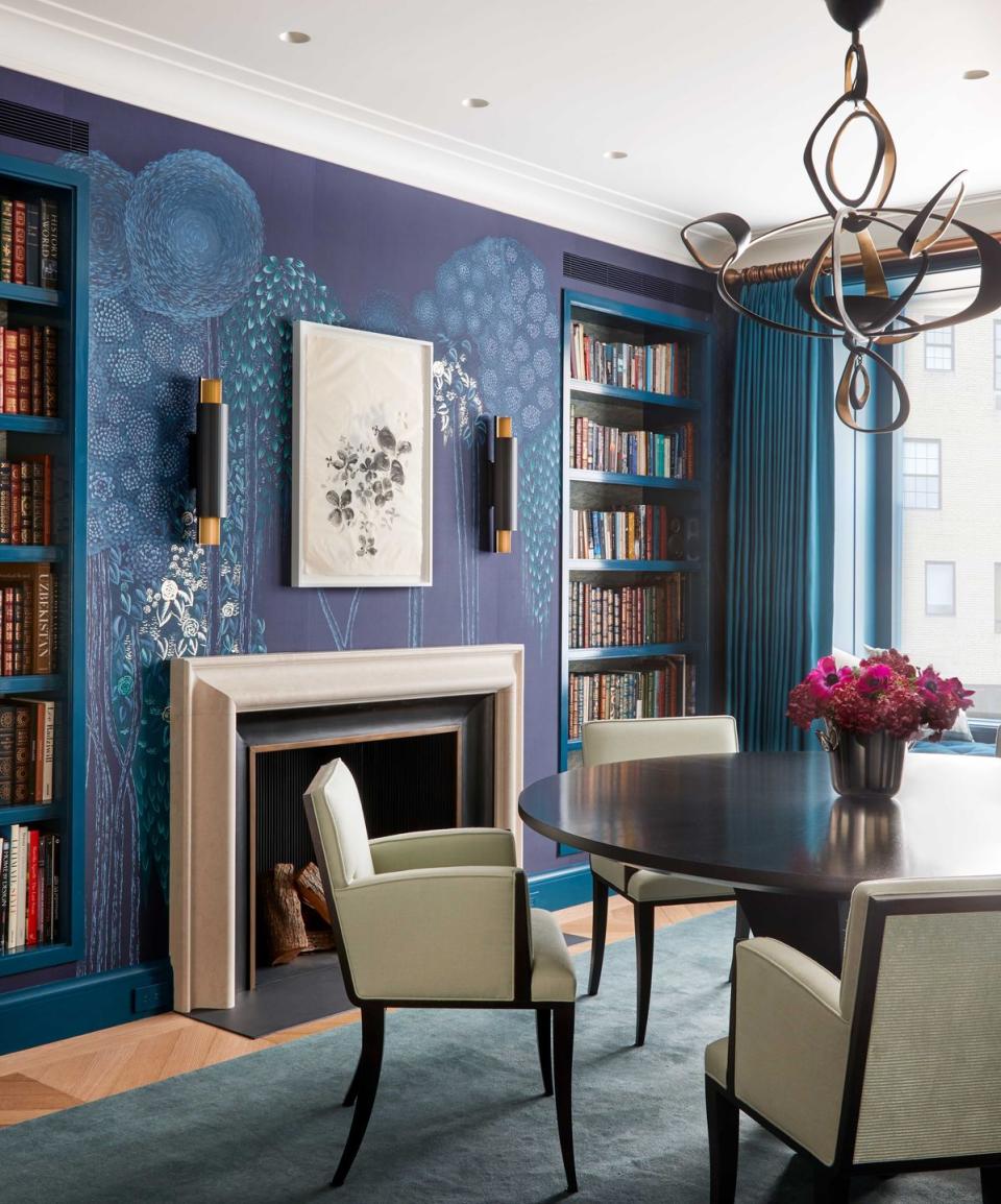 a blue dining room with a round table surrounded by three upholstered chairs and a swirling metal light fixture hanging above