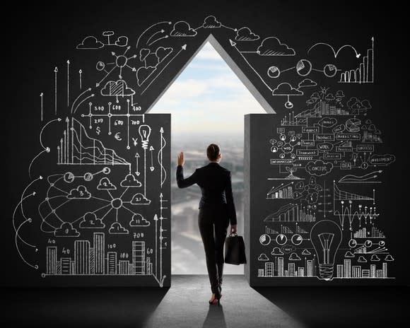 Woman in business suit walking through a wall opening shaped like an upward-pointing arrow.