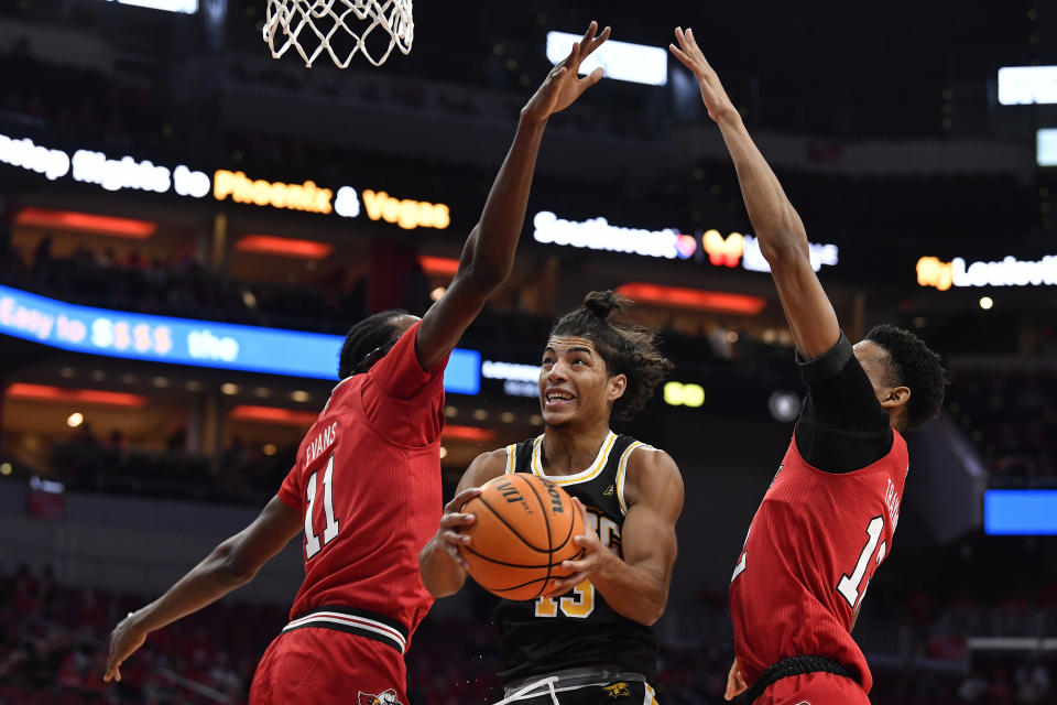 Maryland Baltimore County guard Dion Brown (13) goes under the defense of Louisville center Dennis Evans (11), and forward JJ Traynor (12) during the first half of an NCAA college basketball game in Louisville, Ky., Monday, Nov. 6, 2023. (AP Photo/Timothy D. Easley)
