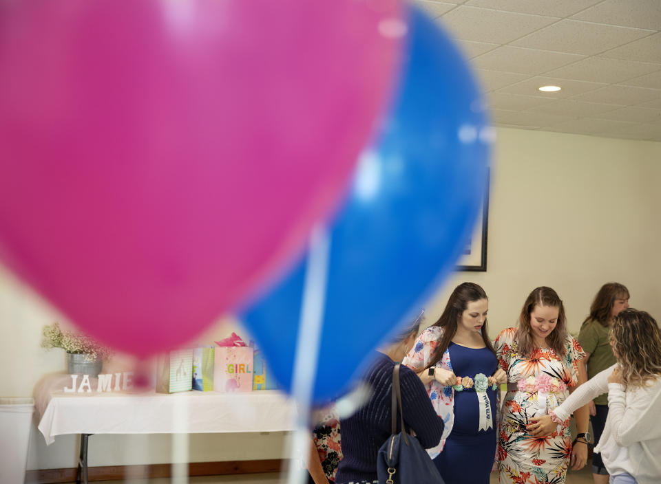 Corri VanDerzee, 19, right, touches the belly of her pregnant sister, Krista Johnston, 24, during a joint baby shower for Johnston and her friend Courtney Nichols, left, at the American Legion hall in Trumansburg, N.Y., Sunday, Sept. 1, 2019. One weekend morning at the legion hall, 24-year-old Krista watched the time-honored military traditions pay tribute to her husband who was killed in Afghanistan. The next day, the hall had been transformed for a baby shower as Krista wore a Hawaiian floral dress with a white-and-gold "mother-to-be" ribbon tied around her midsection. (AP Photo/David Goldman)