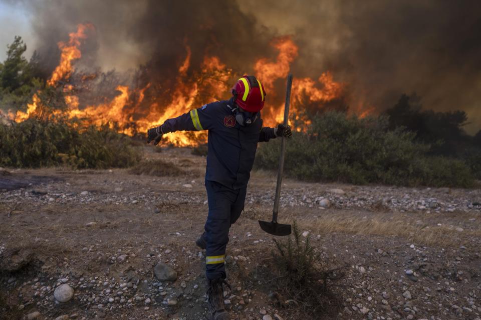 A firefighter leaves as the flames approaching him during a wildfire in Vati village, on the Aegean Sea island of Rhodes, southeastern Greece, on Tuesday, July 25, 2023. A third successive heat wave in Greece pushed temperatures back above 40 degrees Celsius (104 degrees Fahrenheit) across parts of the country Tuesday following more nighttime evacuations from fires that have raged out of control for days. (AP Photo/Petros Giannakouris)