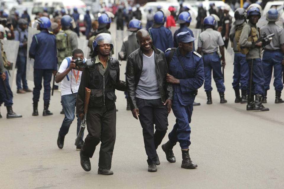 An opposition party supporter smiles after being arrested by police while gathered to hear a speech by the country's top opposition leader in Harare, Wednesday, Nov. 20, 2019. Zimbabwean police with riot gear fired tear gas and struck people who had gathered at the opposition party headquarters to hear a speech by the main opposition leader Nelson Chamisa who still disputes his narrow loss to Zimbabwean President Emmerson Mnangagwa. (AP Photo/Tsvangirayi Mukwazhi)