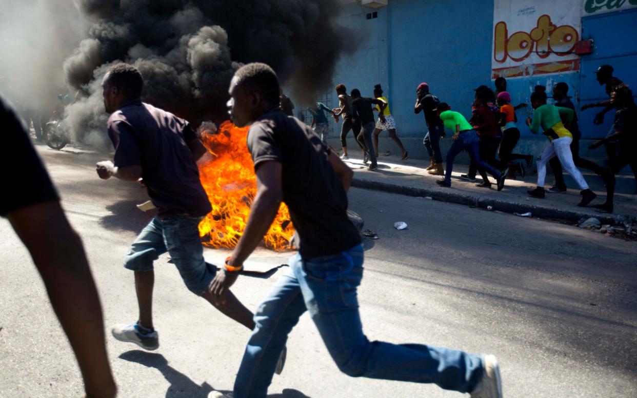 Protesters run past a barricade to a nearby depot that was being looted, during a protest demanding the resignation of President Jovenel Moise in Port-au-Prince, Haiti - AP