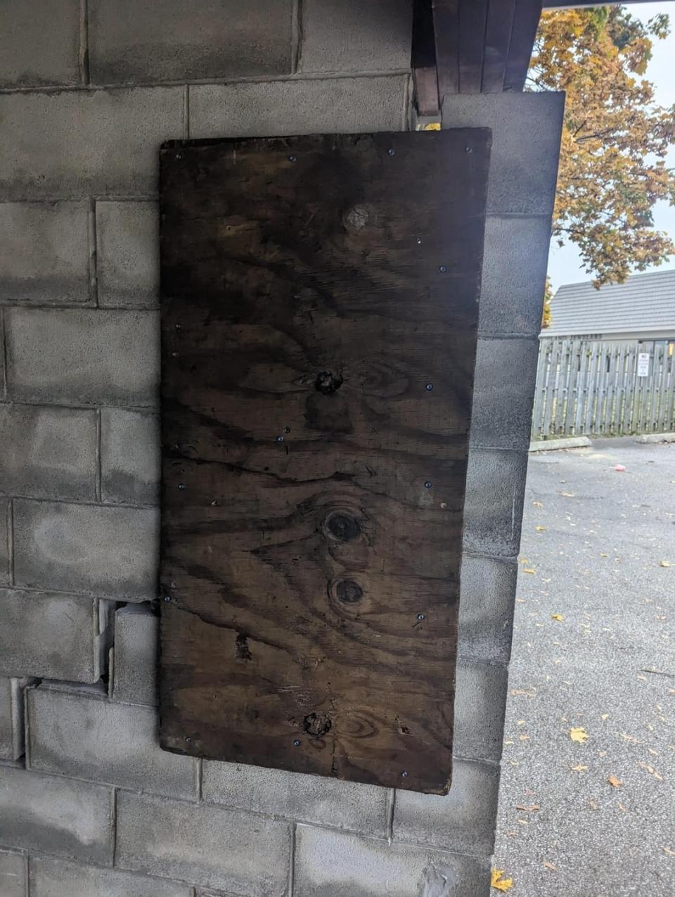 Wooden board with multiple knots fixed to a brick wall, covering something behind it