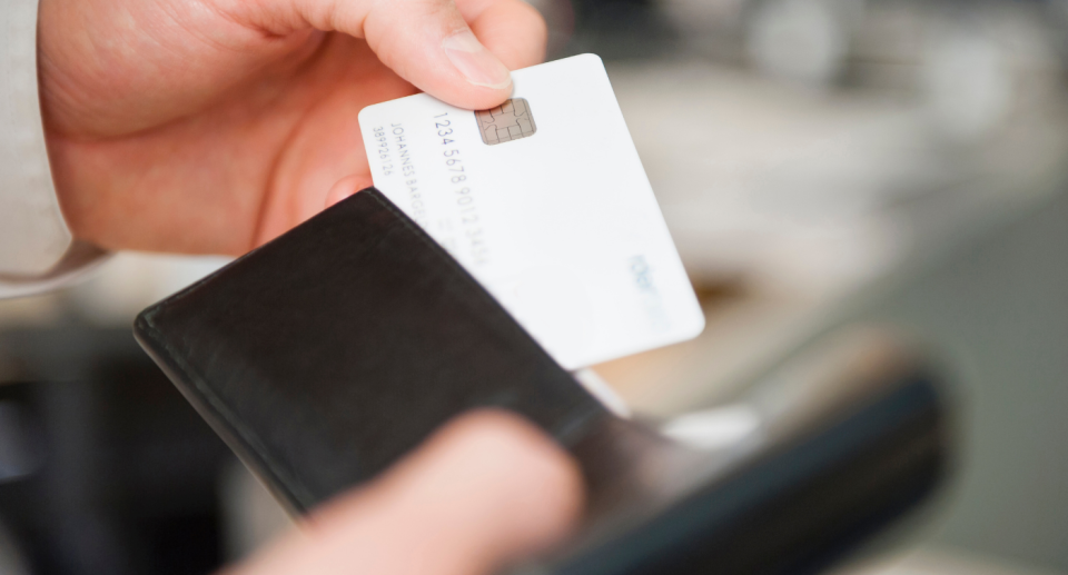 man holding white bank card and brown leather wallet