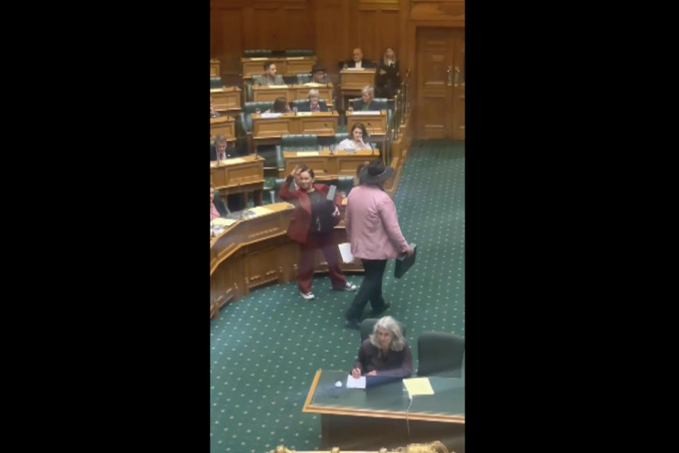 In this image from video, Indigenous New Zealand lawmaker Rawiri Waititi, right, leaves Parliament's debating chamber after performing a Maori haka in Wellington, New Zealand, Wednesday, May 12, 2021. Waititi was thrown out of the debating chamber for performing a Maori haka in protest at what he said were racist arguments. Waititi's stance came after ongoing debate among lawmakers about the government's plans to set up a new Maori Health Authority as part of sweeping changes to the health care system. His party's other co-leader, Debbie Ngarewa-Packer is seen at left. (Thomas Coughlan via AP)