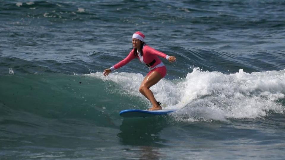 A woman wearing a Santa hat and bathing suit goes surfing on Christmas Day at Bondi Beach in Sydney, Australia, 25 December 2023.