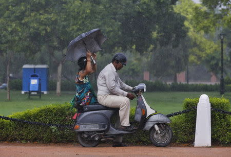 A commuter prepares to park his scooter as his passenger holds an umbrella during a heavy rain shower in New Delhi, June 22, 2015. REUTERS/Adnan Abidi