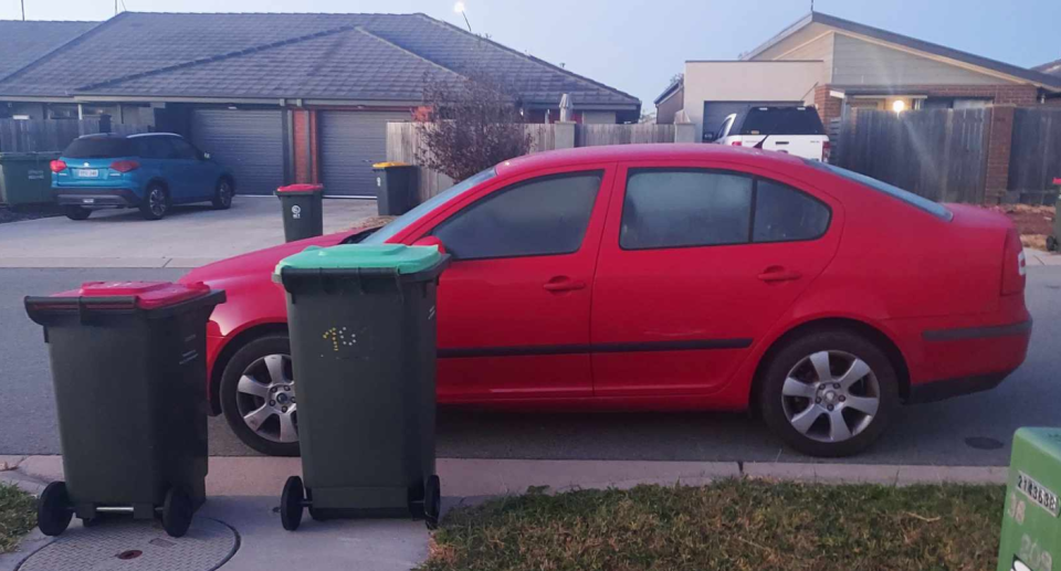 The red car parked in front of the bins.