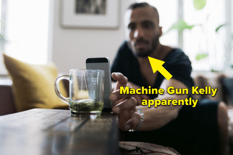 A guy setting up his phone against an empty glass mug with an arrow pointing at him with the caption "Machine Gun Kelly apparently