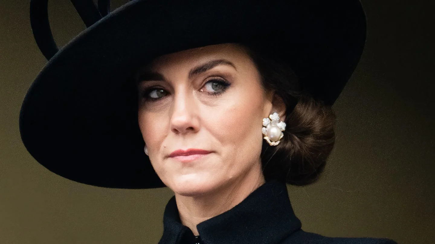 kate middleton, princess of wales looks to the right, she wears a black hat and jacket with large pearl earrings and a pink floral pin on her jacket