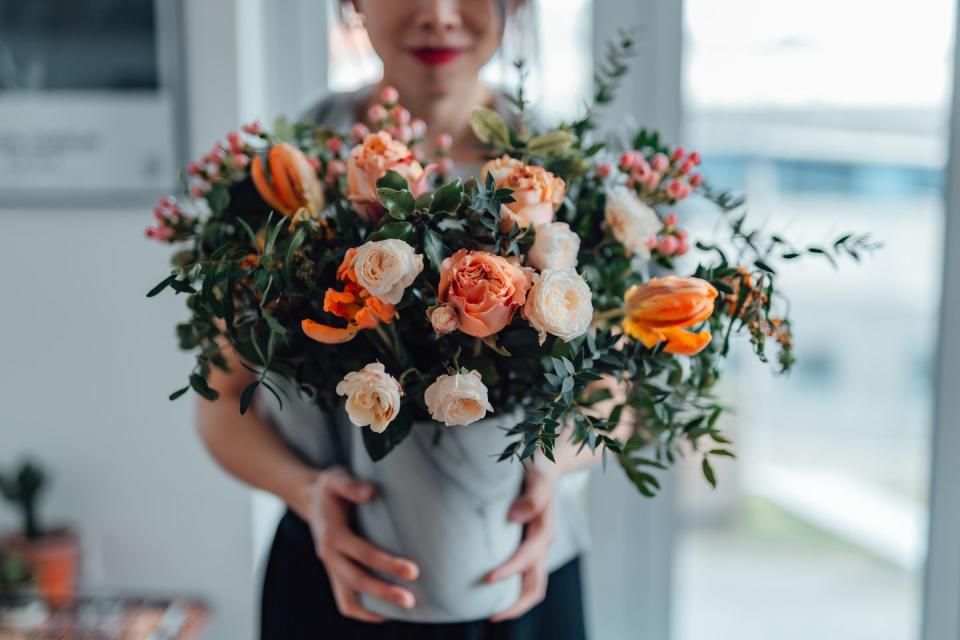 shot of an unrecognisable woman covering her face with flowers in living room