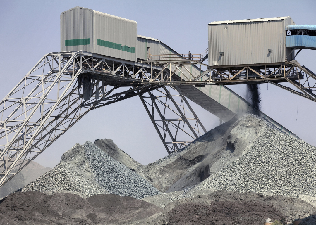 A conveyor belt on a metal frame supported by tall legs with large piles of rocks underneath.