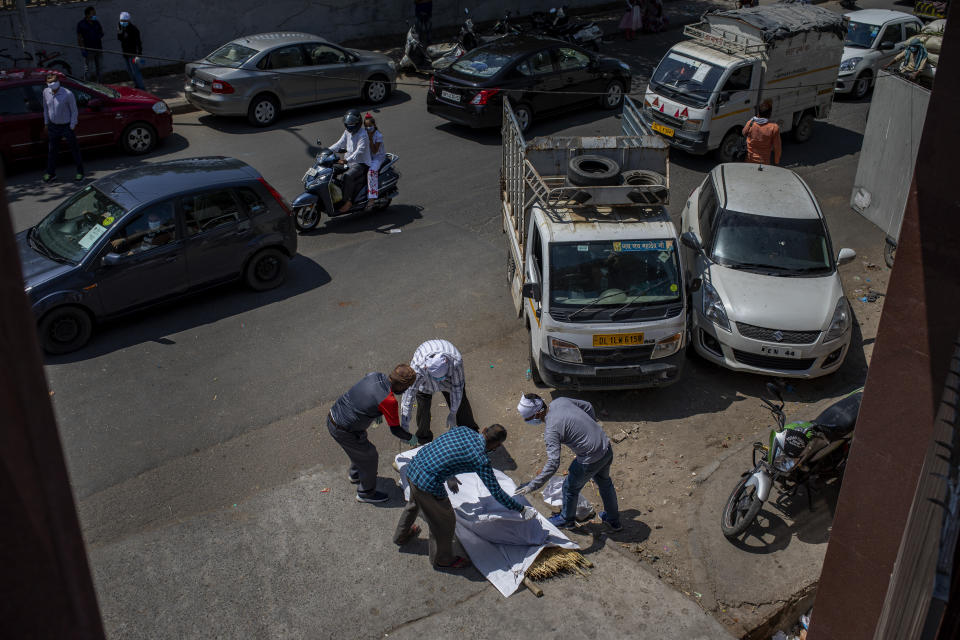 Members of the family of a COVID-19 victim put a shroud over the body lying on a road outside a crematorium in New Delhi, India, Saturday, April 24, 2021. Delhi has been cremating so many bodies of coronavirus victims that authorities are getting requests to start cutting down trees in city parks, as a second record surge has brought India's tattered healthcare system to its knees. (AP Photo/Altaf Qadri)