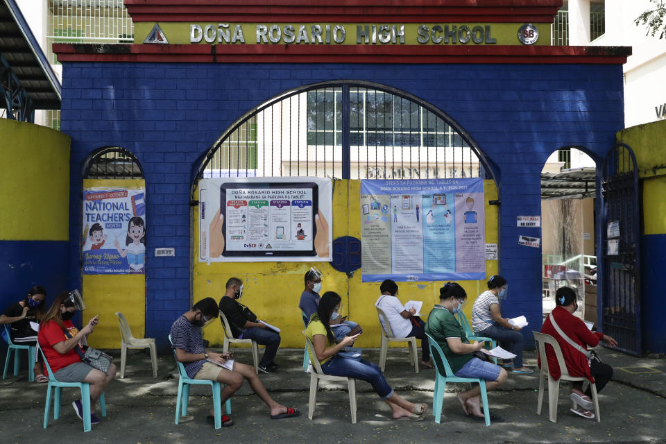 People wearing masks and face shields wait for their turn to pick up student electronic tablets as online classes are scheduled to start next week in the Dona Rosario High School in Quezon city, Philippines, Thursday, Oct. 1, 2020. Public schools will hold online classes using electronic gadgets and educational materials provided to students as the opening got delayed due to the coronavirus pandemic. (AP Photo/Aaron Favila)