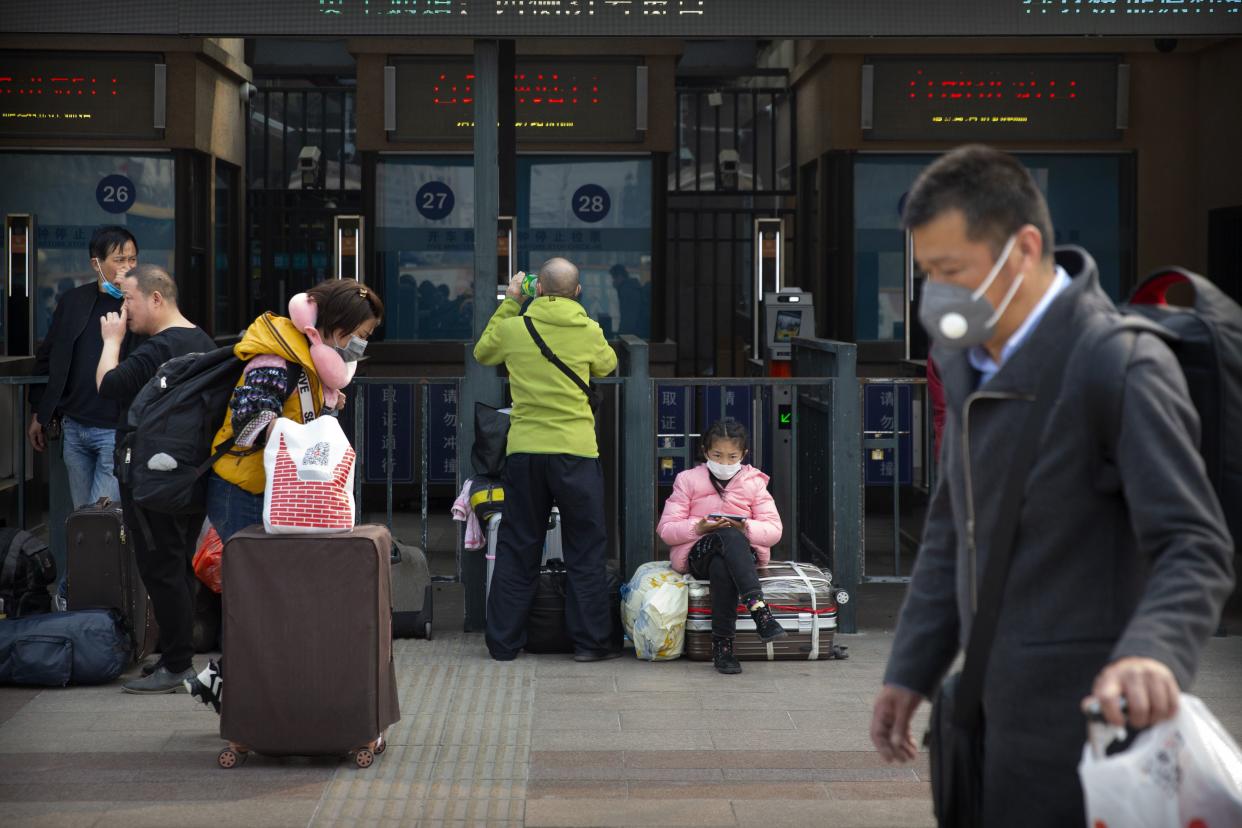Travelers wearing face masks walk outside the Beijing Railway Station in Beijing on March 25, 2020. Some train stations and bus services reopened in China's Hubei Province on Wednesday and people who passed a health check would finally be allowed to travel for the first time since the coronavirus outbreak surged in January.