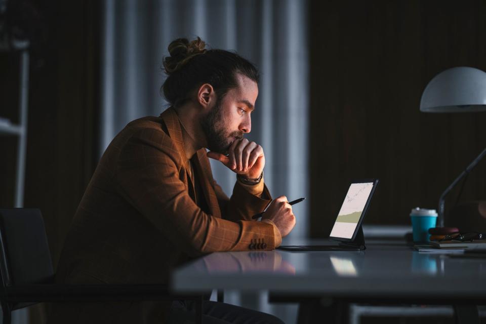 A person in a darkened room looking at stock charts on a tablet.