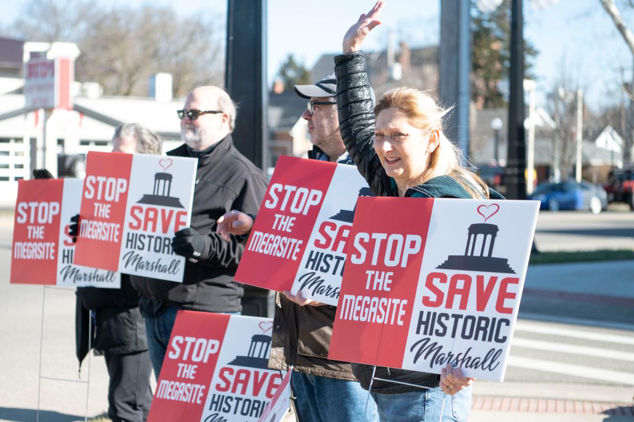Marshall resident Linda Smoot waves at passing cars while protesting development of the Marshall Megasite in downtown Marshall on Monday, Feb. 13, 2023.