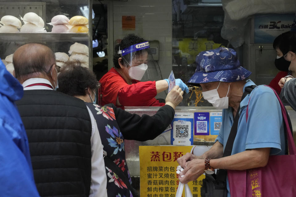 People wearing face masks line up to buy lunch boxes for take-away orders at a shop in Hong Kong, Sunday, March 13, 2022. The territory's leader, Chief Executive Carrie Lam, warned the peak of the latest surge in coronavirus infections might not have passed yet. (AP Photo/Kin Cheung)