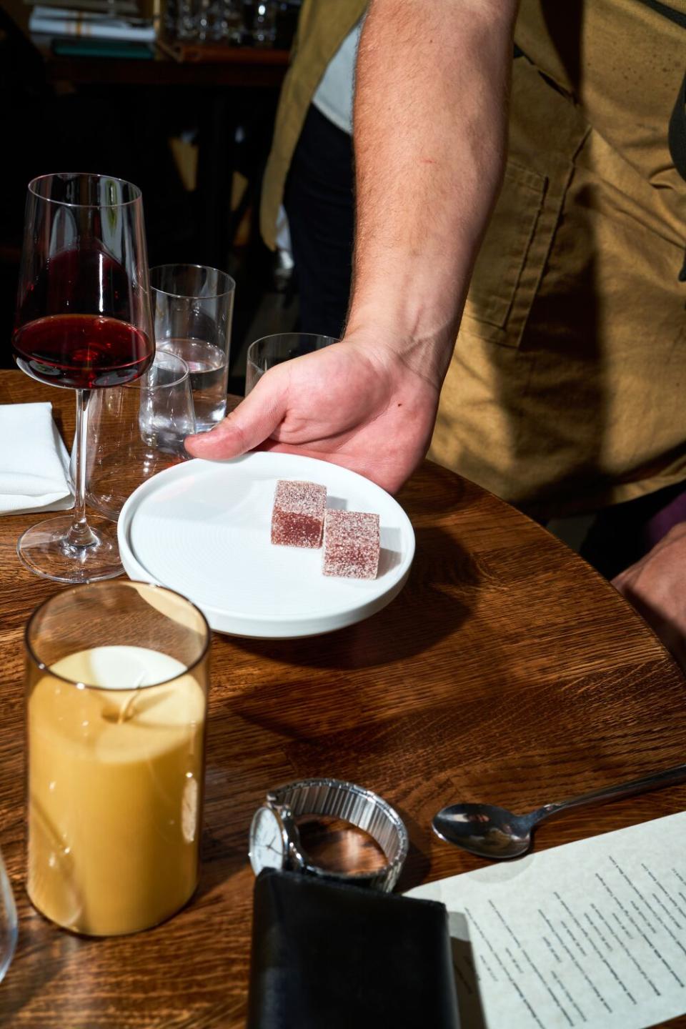 A hand holds a plate containing two white-dusted red cubes of dessert.