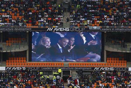 U.S. President Barack Obama (C) and his wife Michelle are seen on a big screen at the First National Bank (FNB) Stadium, also known as Soccer City, during the national memorial service for former South African President Nelson Mandela in Johannesburg December 10, 2013. World leaders from Obama to Cuba's Raul Castro joined thousands of South Africans to honour Nelson Mandela on Tuesday in a memorial that will celebrate his gift for uniting enemies across political and racial divides. REUTERS/Yves Herman