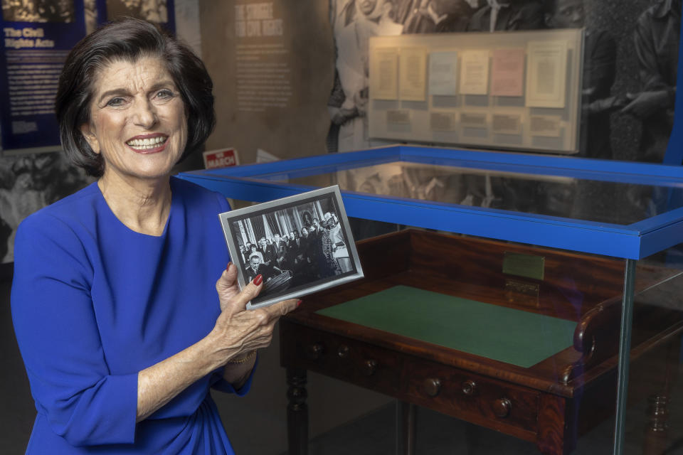 Luci Baines Johnson holds a photo taken during the signing of the Voting Rights Act of 1965, during an interview at the LBJ Presidential Library, on May 16, 2023, in Austin, Texas. Johnson is standing behind her father President Lyndon B. Johnson. Luci Baines Johnson was a somewhat impatient 18-year-old on Aug. 6, 1965, when she happened to be on what she called "daddy duty," meaning "I was supposed to accompany him to important occasions." (AP Photo/Stephen Spillman, File)