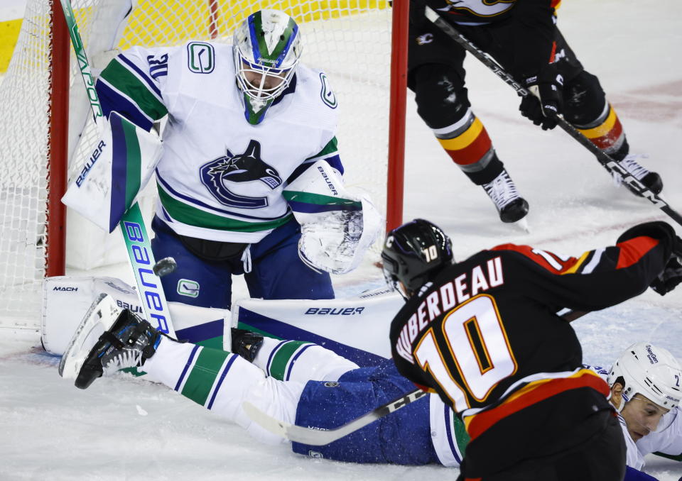 Vancouver Canucks defenseman Luke Schenn, right, attempts to block as shot from Calgary Flames forward Jonathan Huberdeau, center, as goalie Spencer Martin stops it during the first period of an NHL hockey game in Calgary, Alberta on Wednesday, Dec. 14, 2022. (Jeff McIntosh/The Canadian Press via AP)