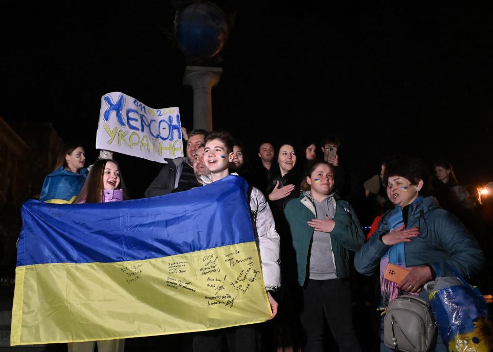 People hold a Ukranian flag and a slogan which reads ‘11/11/2022 - Kherson - Ukraine' in Maidan Square to celebrate the liberation of Kherson, in Kyiv on 11 November 2022, amid the Russian invasion of Ukraine (AFP via Getty Images)