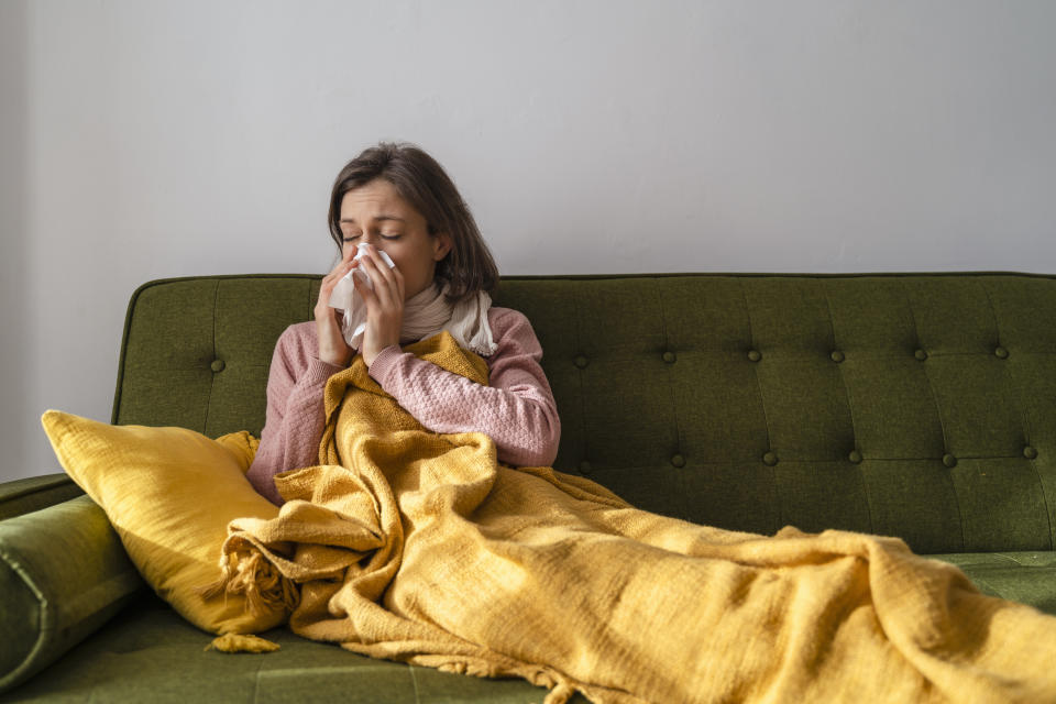 Erkältete Frau unter Decke auf Sofa