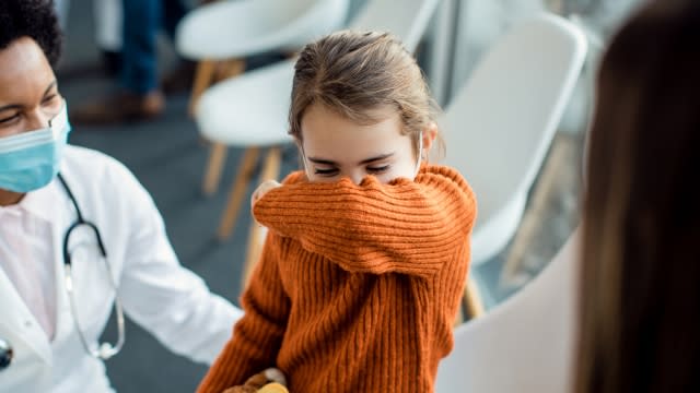 A toddler coughs into her arm.