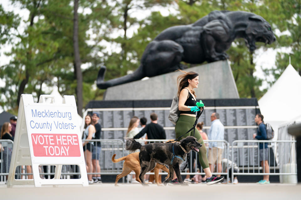 A woman walks with dogs past a sign identifying a polling location on the final day of early voting at Bank of America Stadium on Nov. 5, 2022, in Charlotte, North Carolina.
