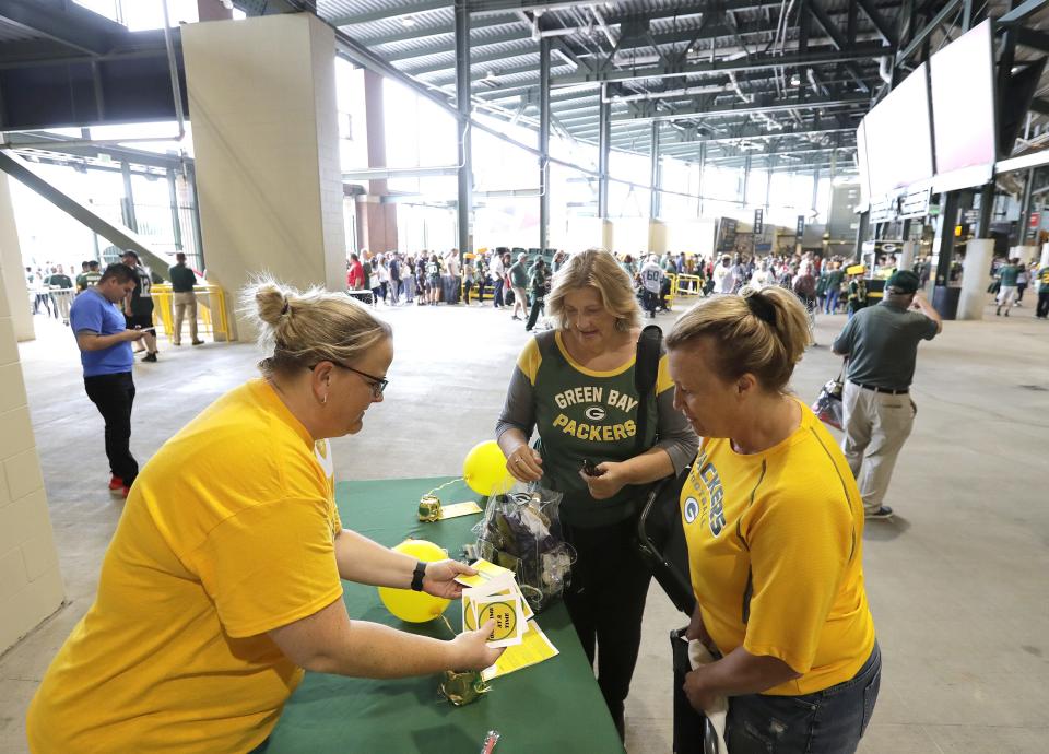 Volunteer Laura Marie John, left, offers stickers to Heather Hougard and Carrie Puzen, both of Green Bay, at the Section Yellow table prior to the Green Bay Packers-Chicago Bears game Sept. 18 at Lambeau Field.