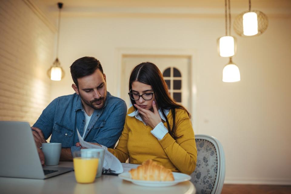 couple eating breakfast looking at laptop and papers concerned