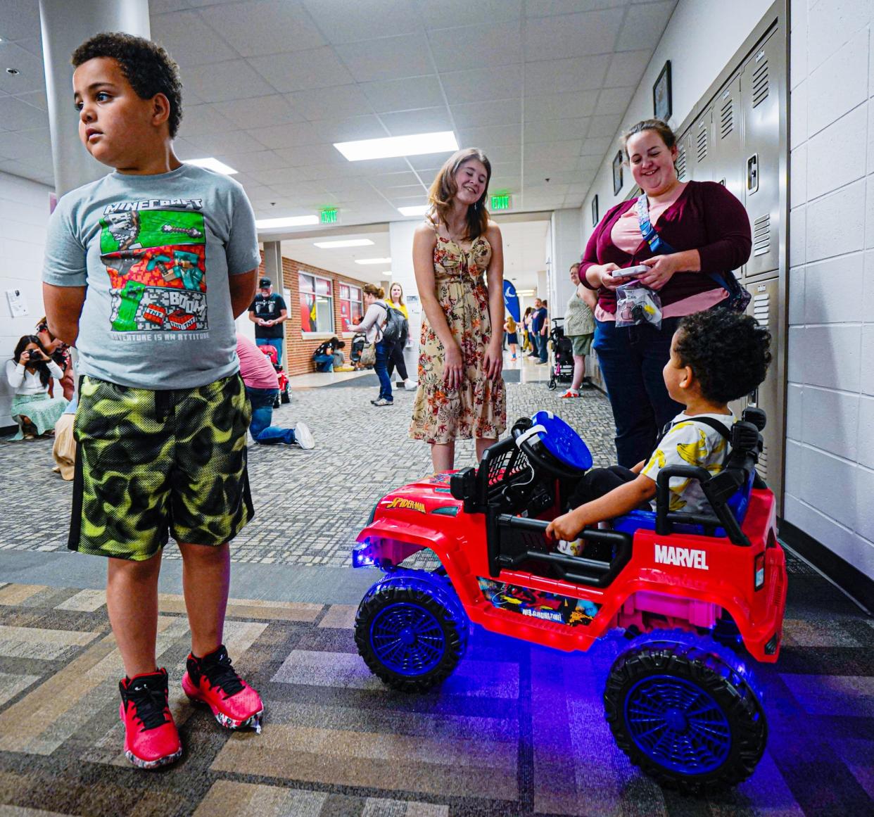 Katie Essex, 17, the founder of the "Mini-Movers" club, center, checks in with the Young family, mom, Rebecca, right, Zeke, in his new customized ride-on electric car, and Liam,  during a "Night of Engineering" on Wednesday, May 10, 2023, at Southport High School in Indianapolis. The "Mini-Movers" club presents children with mobility issues, custom modified ride-on electric cars to fit their mobility needs. 