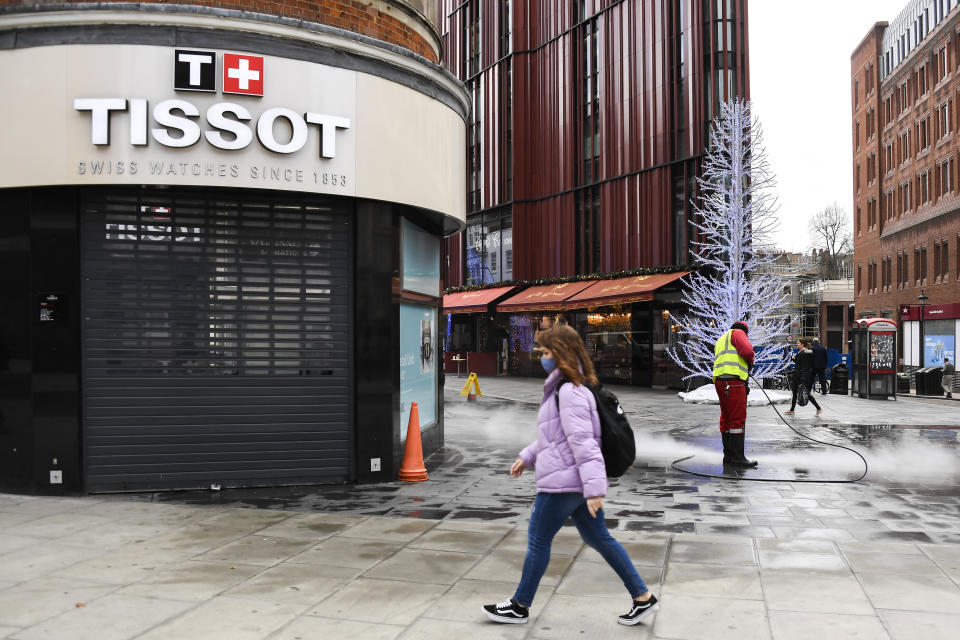 A woman walks past a closed shop while a man cleans the deserted pavement near Oxford Street in London on Tuesday. Oxford Street, one of Europe's busiest shopping zones, would usually be packed in the weeks before Christmas. (Photo: ASSOCIATED PRESS)